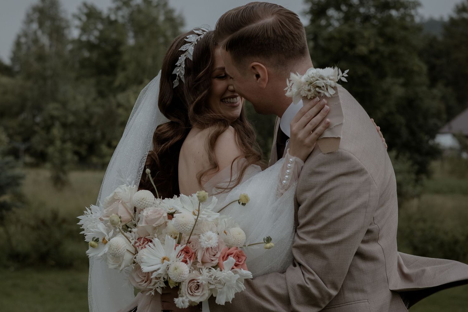 A tender wedding moment captured outdoors with a romantic bouquet of white and blush-colored flowers.