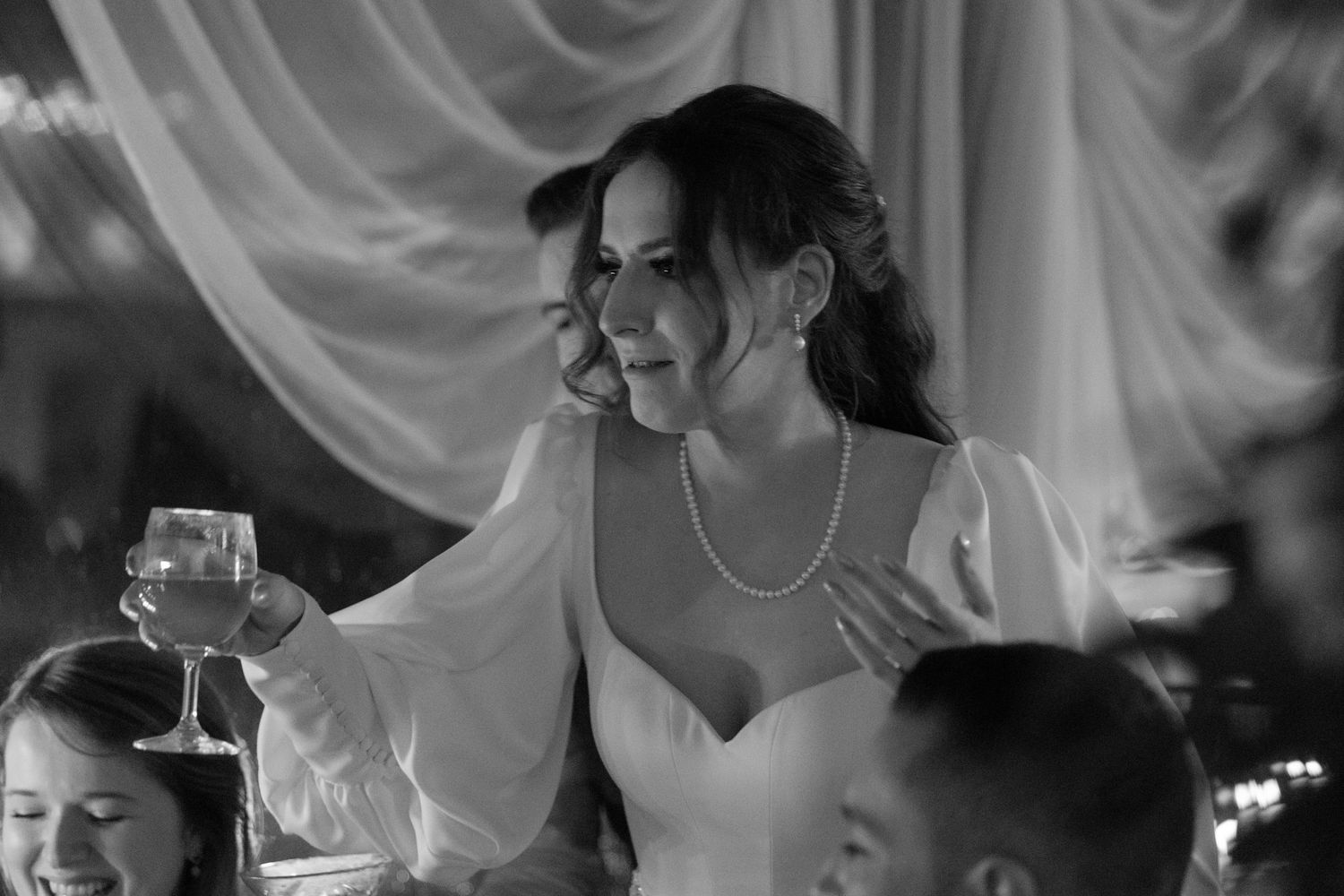 Black and white photo of a bride in a sweetheart neckline dress smiling during a wedding reception celebration.