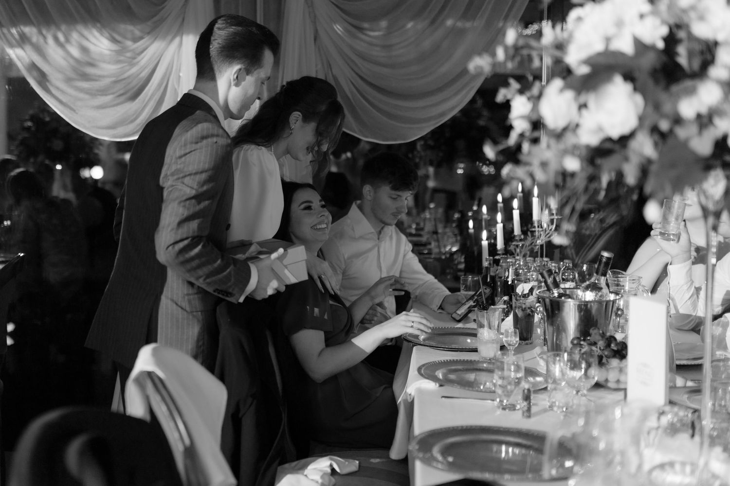 Guests share an intimate black and white moment at an elegant reception with candlelit table settings.