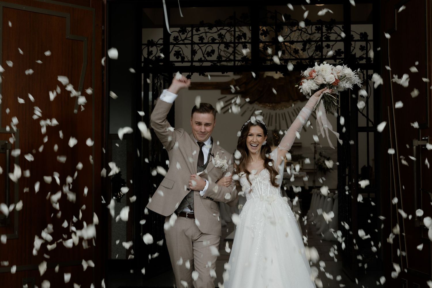 A couple exits their wedding ceremony under a shower of white confetti petals in celebration.