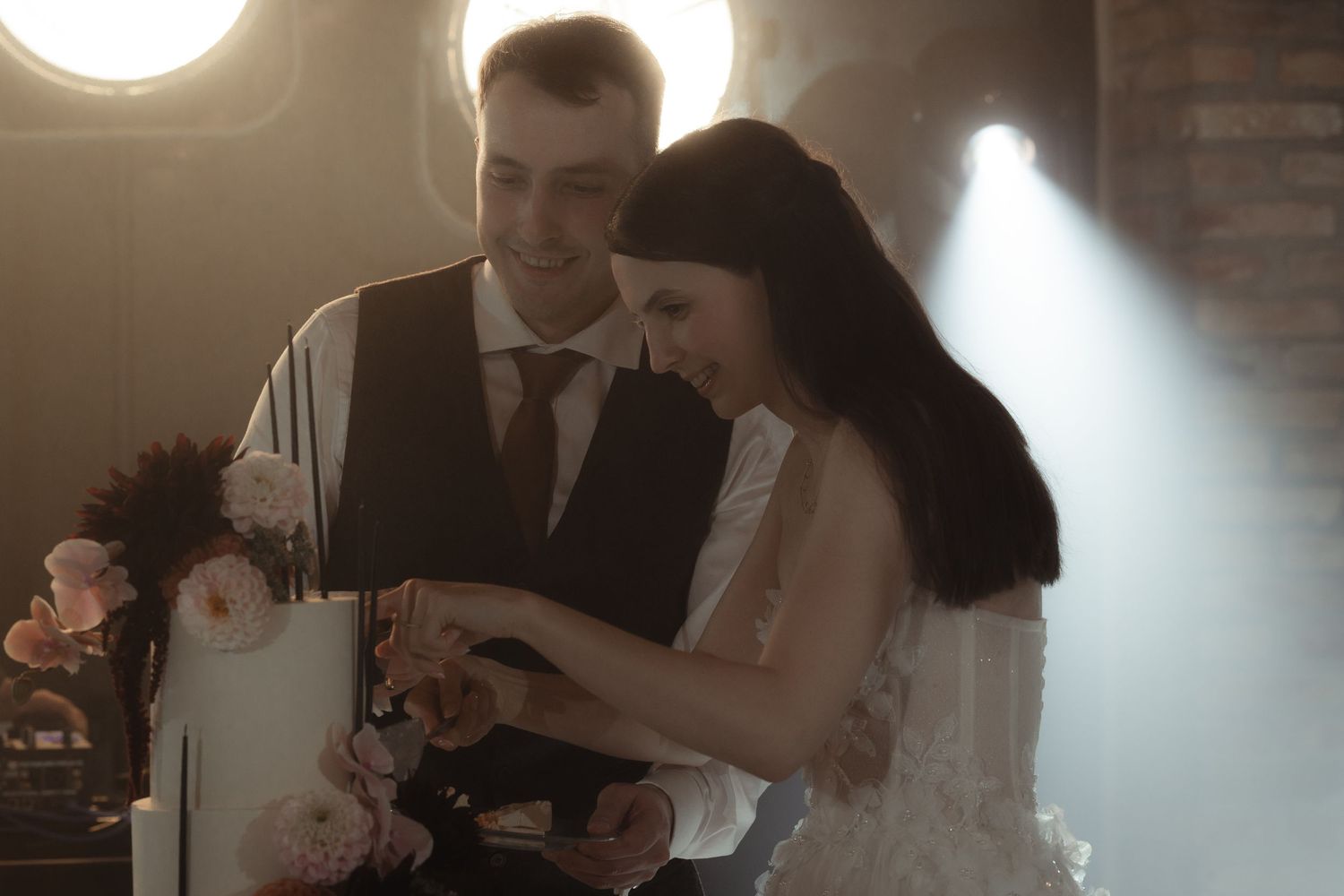A romantic wedding couple shares their first dance in a dimly lit ballroom with soft lighting creating an intimate atmosphere.