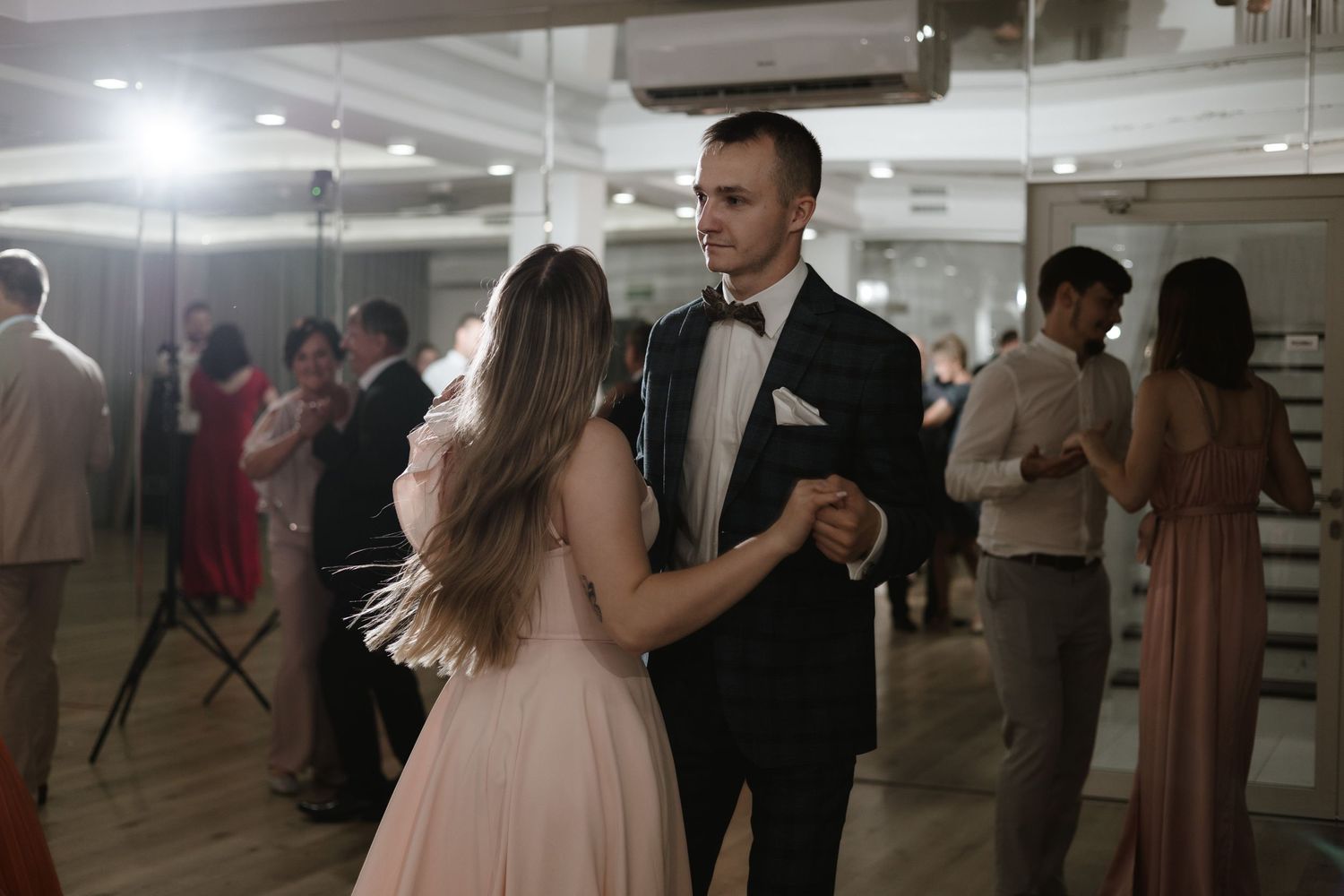 A couple shares a dance at a wedding reception with other guests visible in the background.