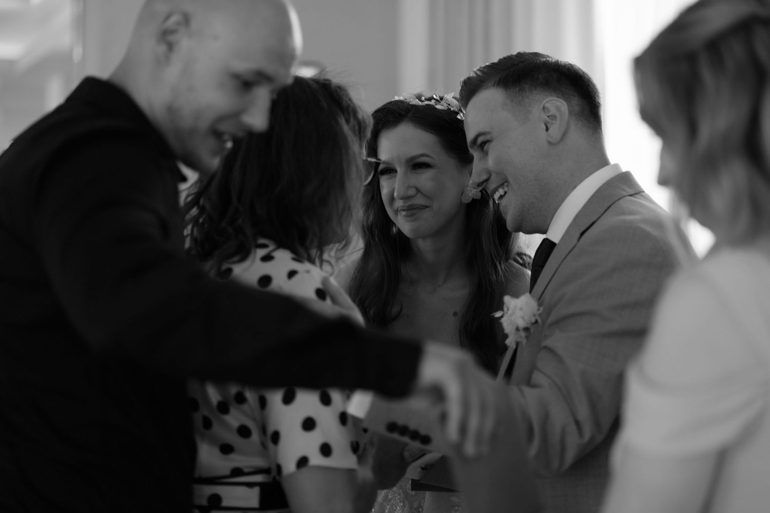 A black and white candid wedding reception moment with guests laughing and socializing together.