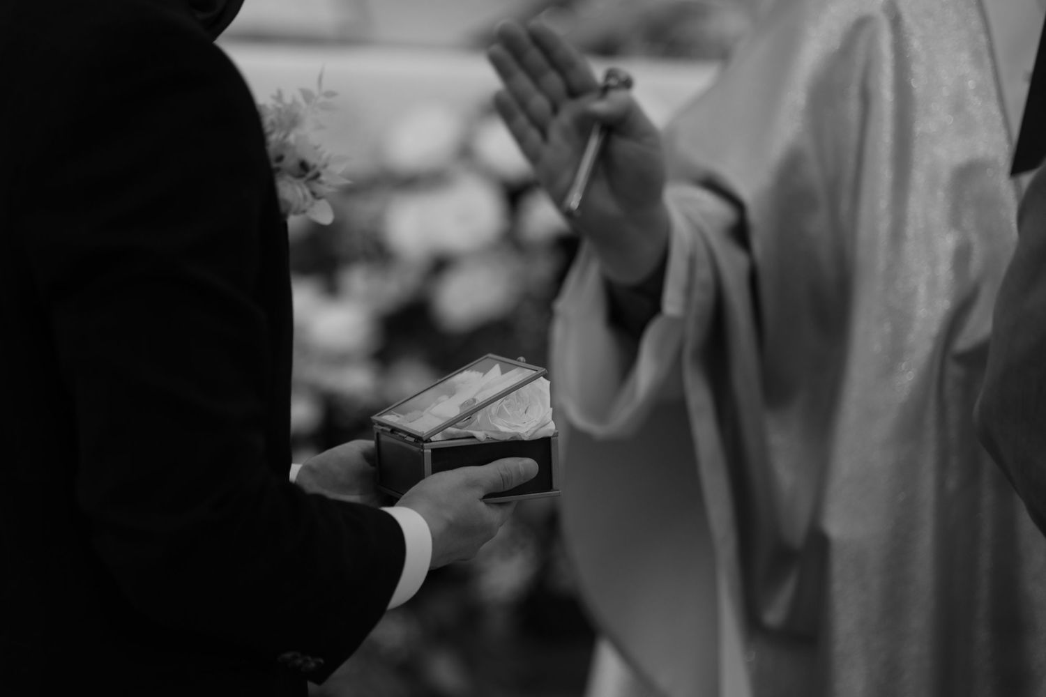 A black and white close-up of hands exchanging rings during a wedding ceremony.