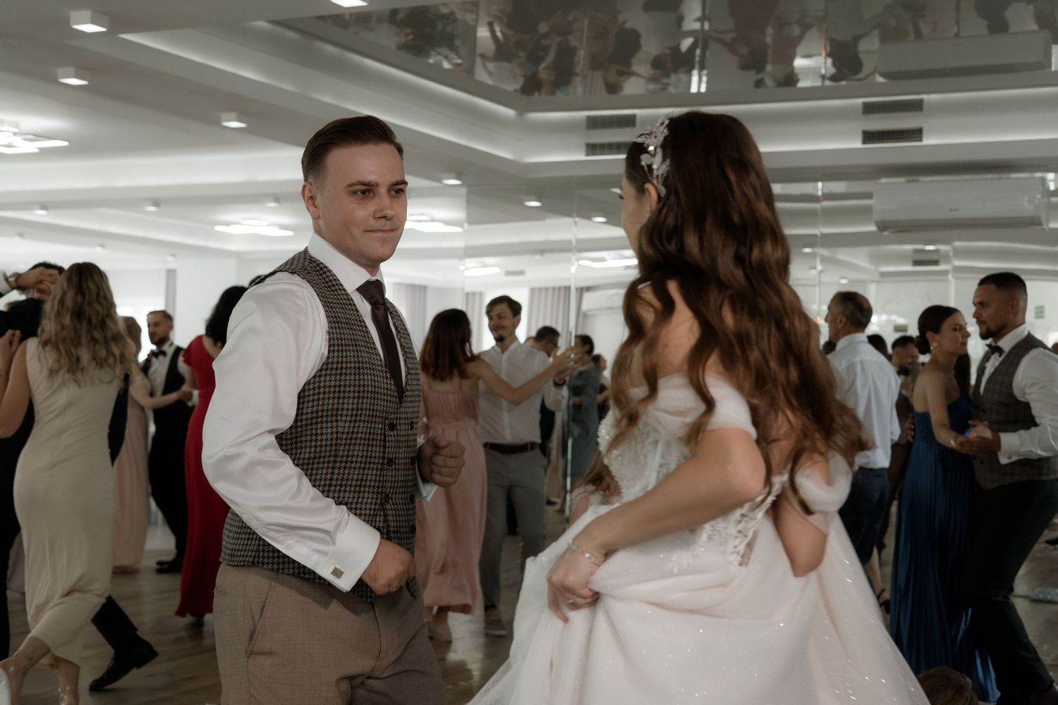 A couple shares a sweet moment at their wedding reception as guests mingle in the background.