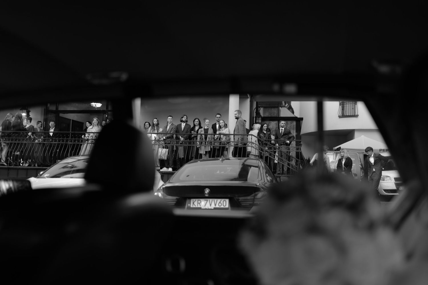 Black and white urban street scene viewed through a car window with pedestrians and vehicles visible in the background.