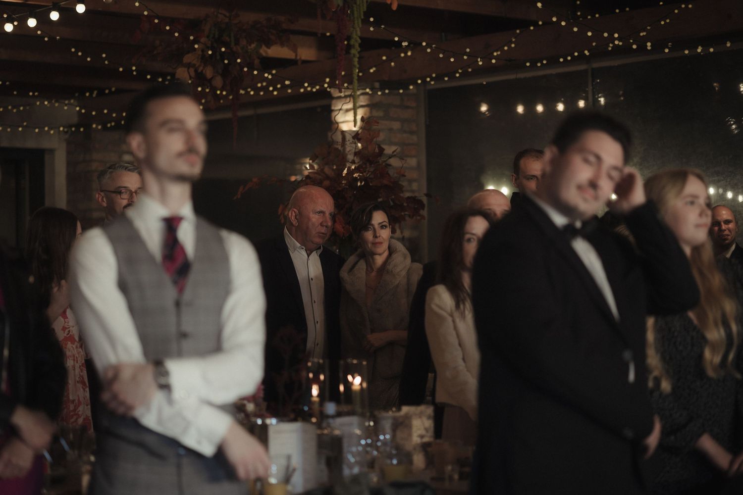 Wedding guests dance and celebrate on a dimly lit dance floor decorated with string lights overhead.