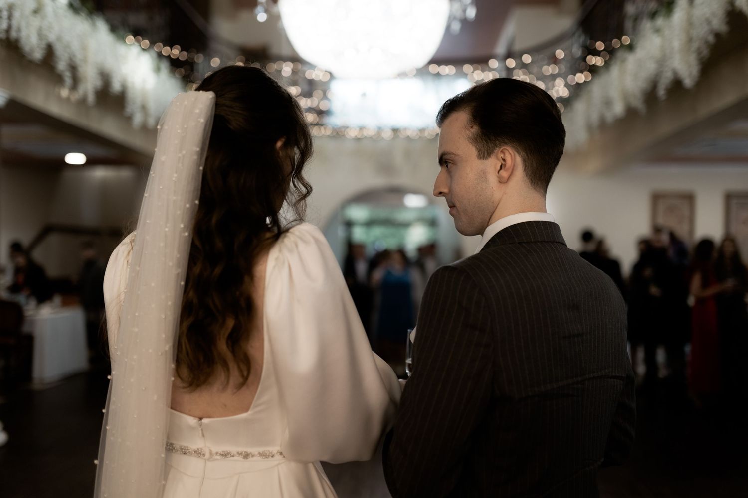 Two people share an intimate moment during a winter wedding celebration beneath decorative lights and white garlands.