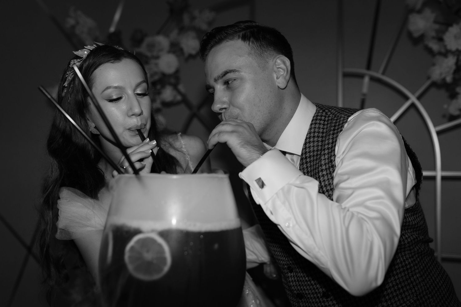 A retro black and white photo of a couple sharing a dark beverage with straws in a vintage-style setting.