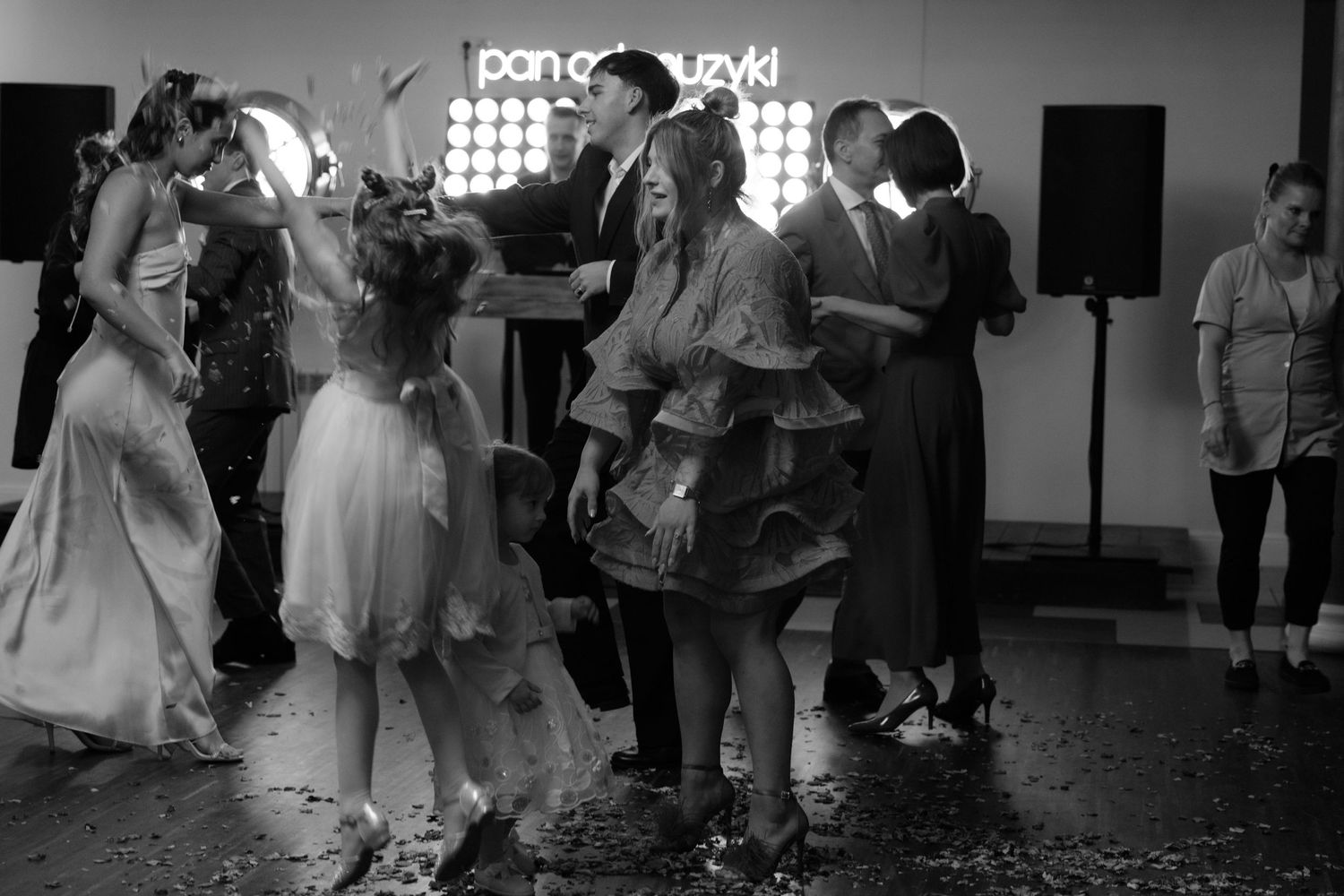 People dancing at a celebration with disco lights and confetti in a black and white photograph.
