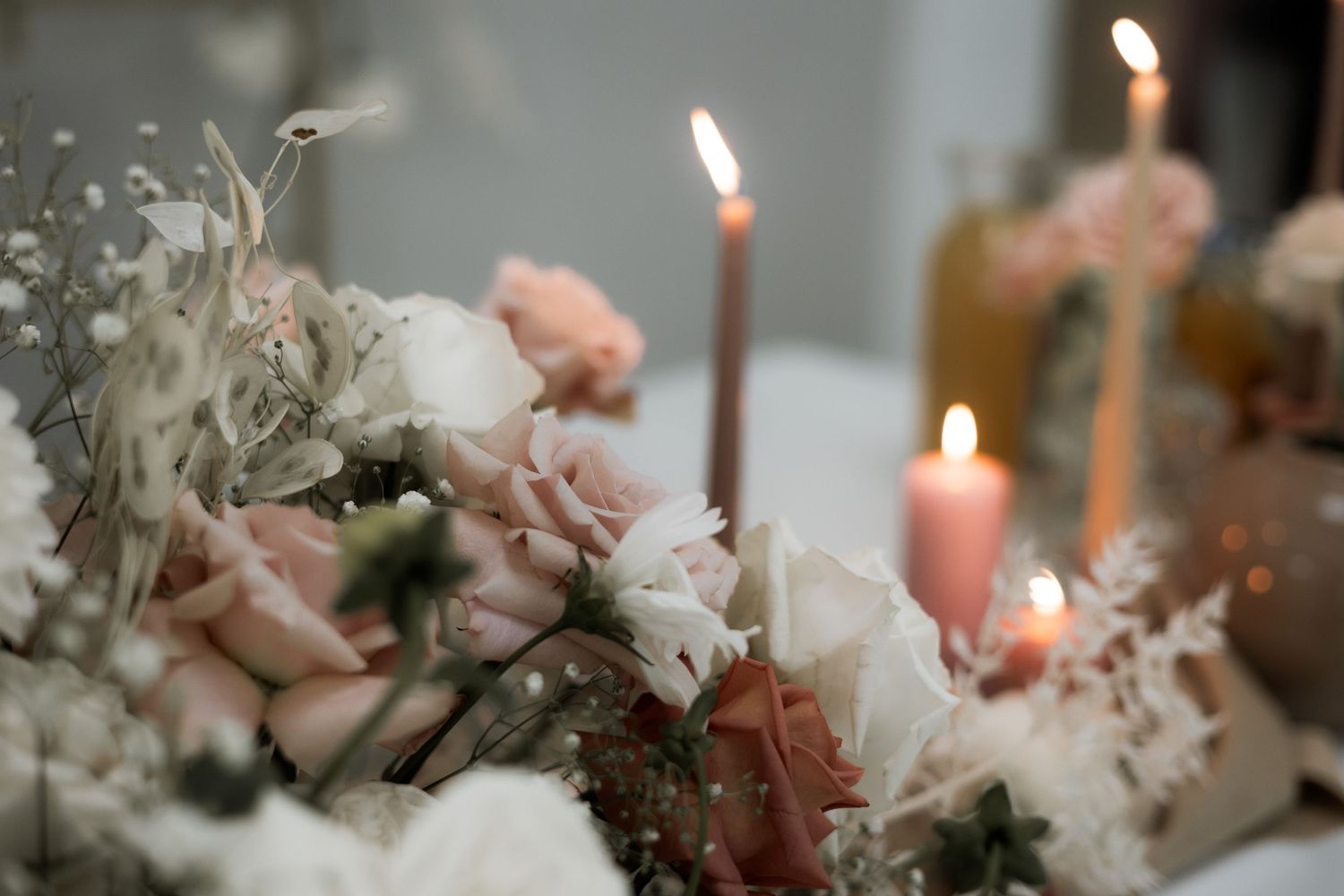 Soft pink and white floral centerpiece with glowing candles on an elegant table setting with a dreamy bokeh effect.