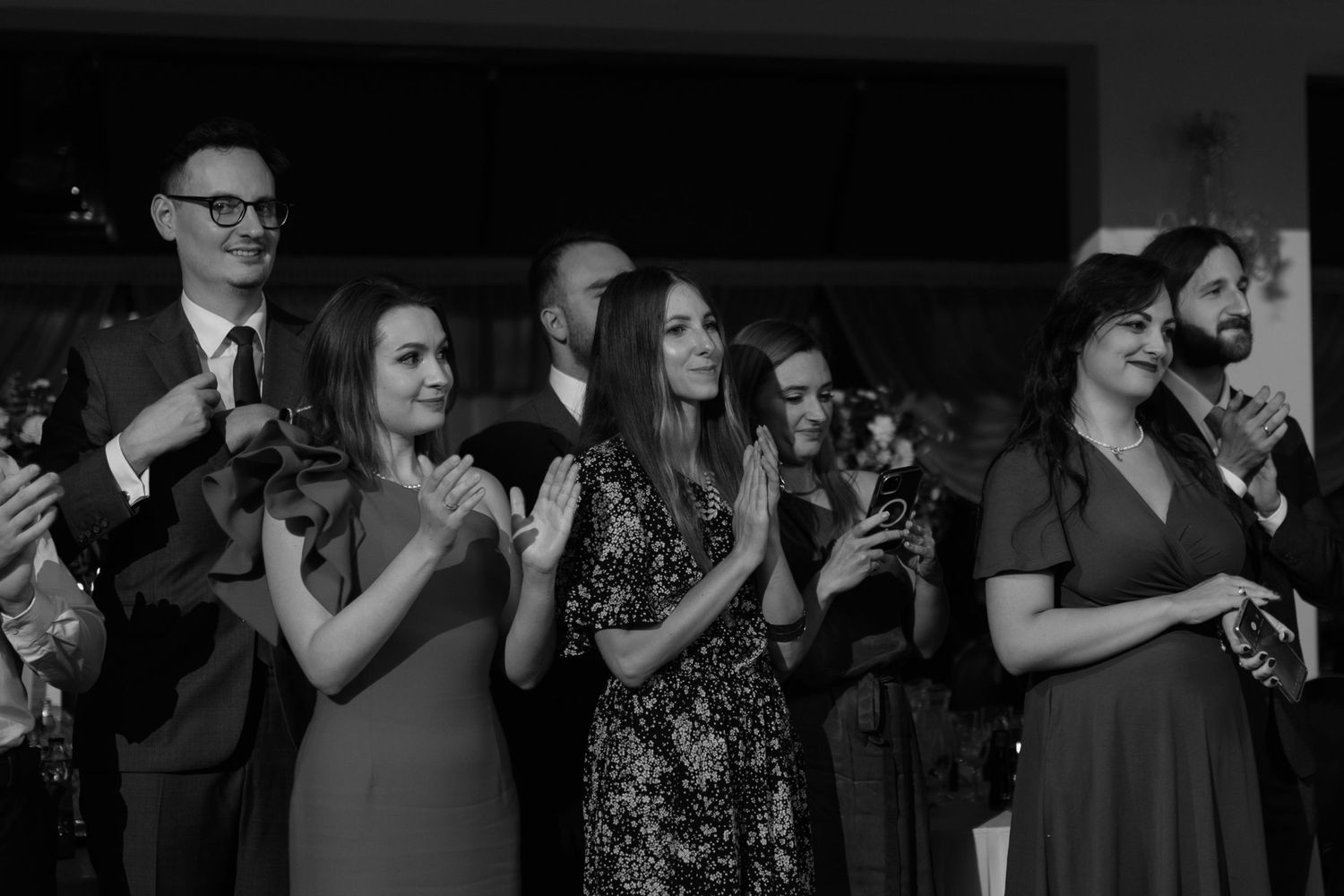 Black and white photograph of a group at an event applauding in formal attire during an indoor celebration.