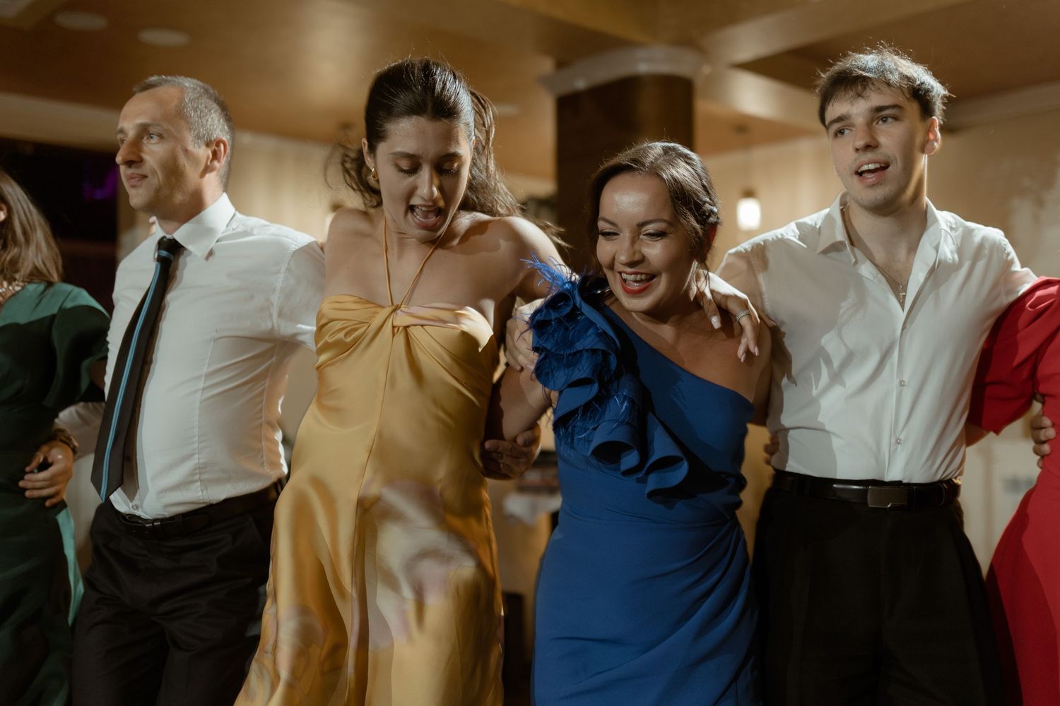 Elegant wedding guests in formal attire including yellow and blue dresses dance and laugh together on the dance floor.