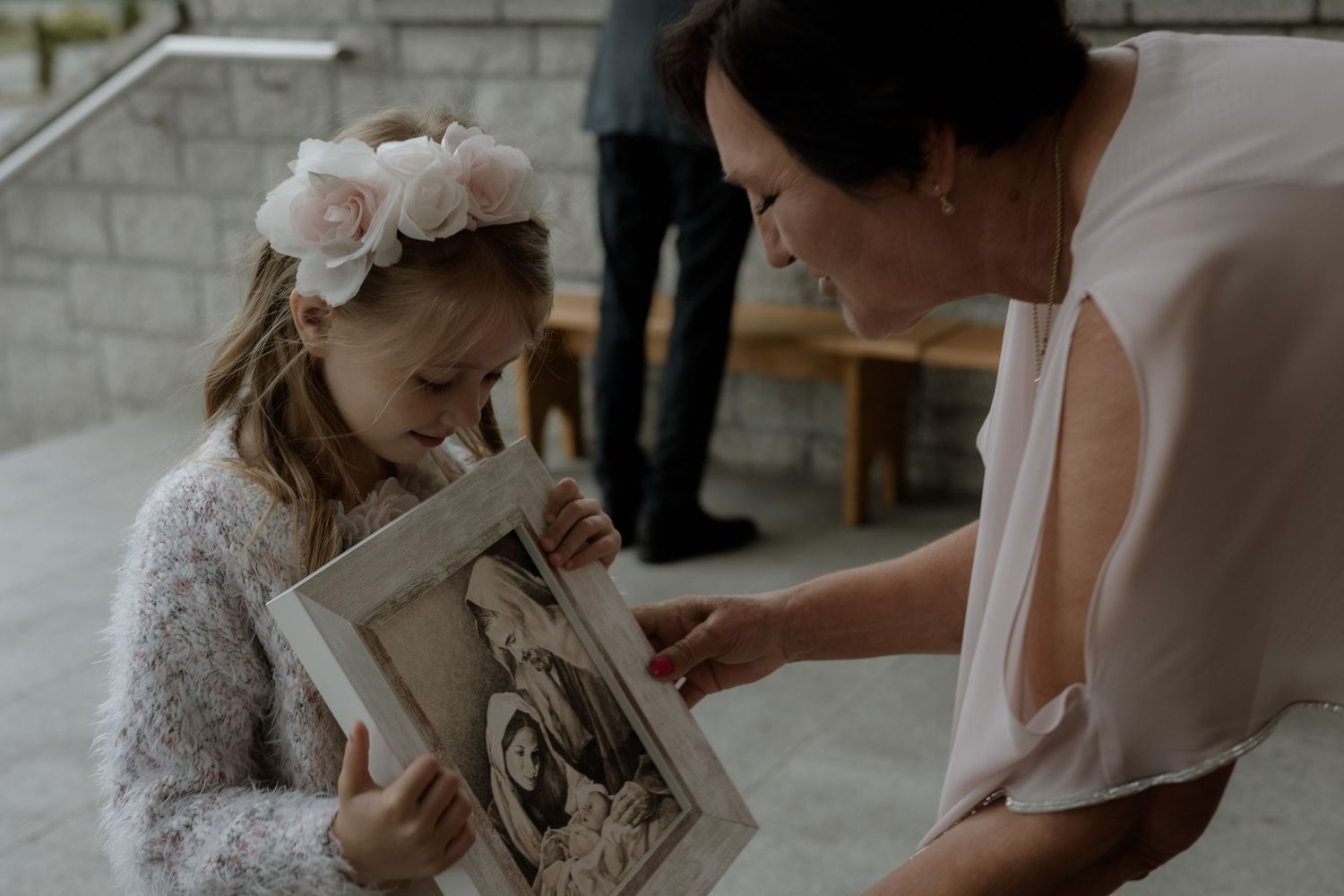 A young girl in a white dress looks at a photo album with a person in a white garment during a special occasion.
