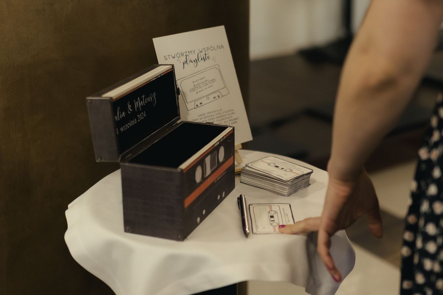 A wooden ring box and cards sit on a white tablecloth while someone holds a polka dot patterned dress.