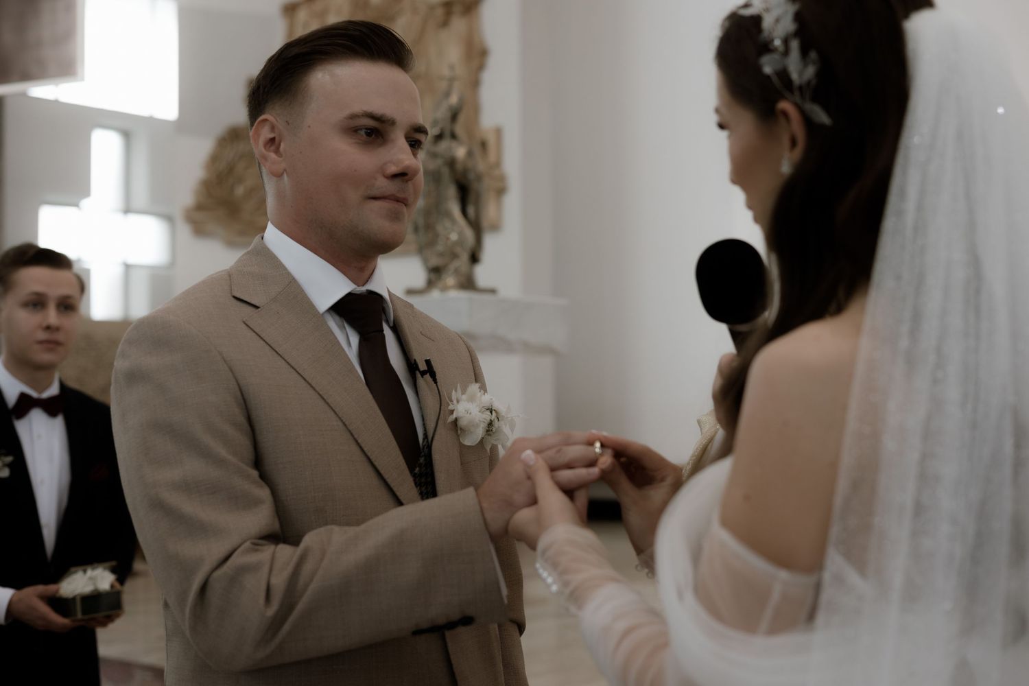 A couple exchanging rings during an indoor wedding ceremony at a bridal altar.
