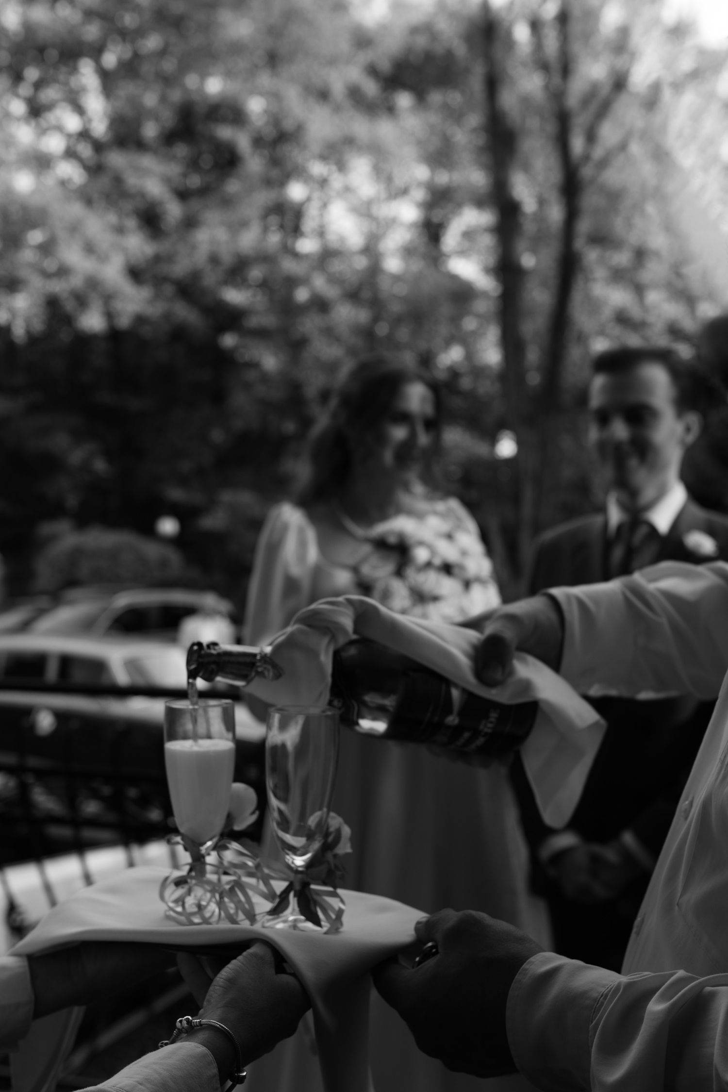 Black and white photo of champagne being poured into glasses at an outdoor celebration.