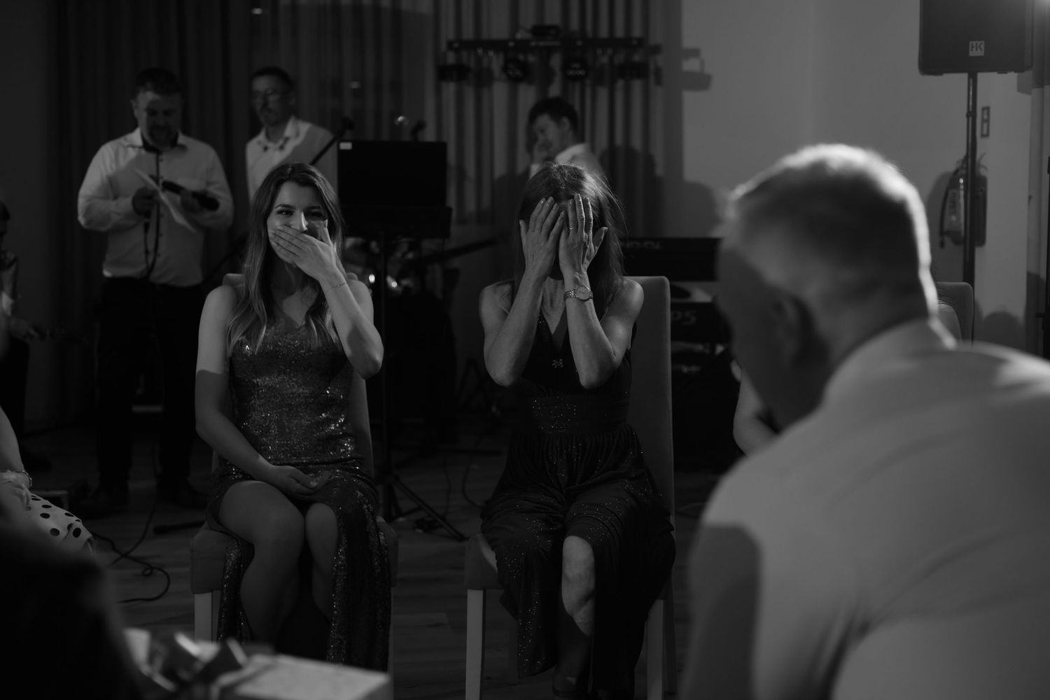 Musicians perform at a dimly lit venue with performers playing harmonicas while others watch in black and white.