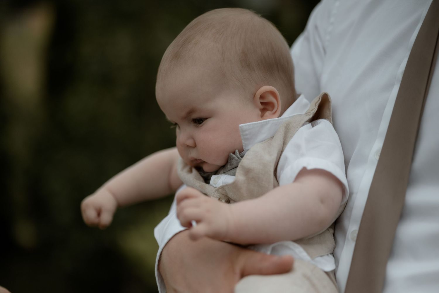 A baby in white clothing sits with a parent outdoors during a peaceful moment in nature.