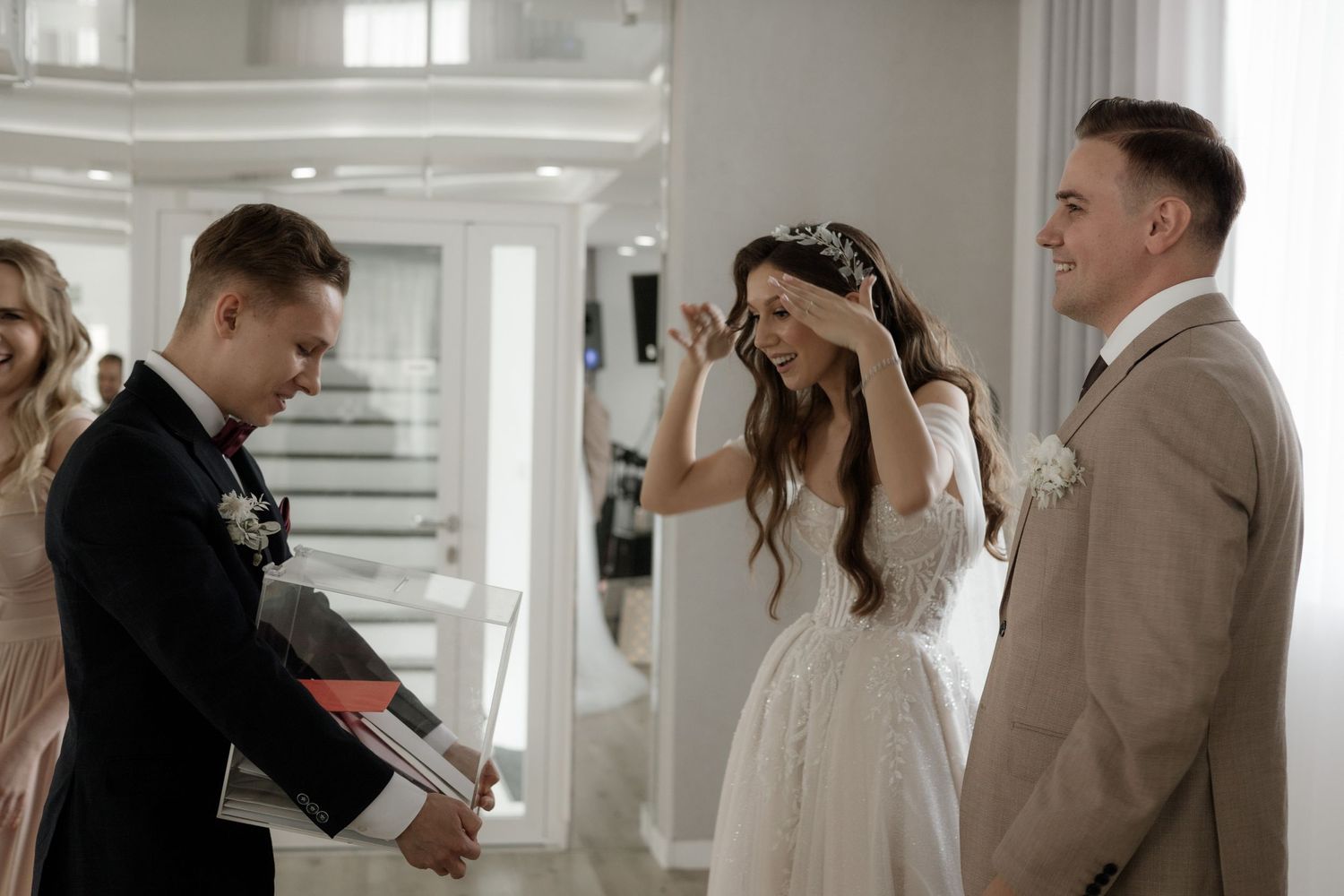 A light-filled wedding scene showing a reaction between guests in formal attire at an indoor venue.