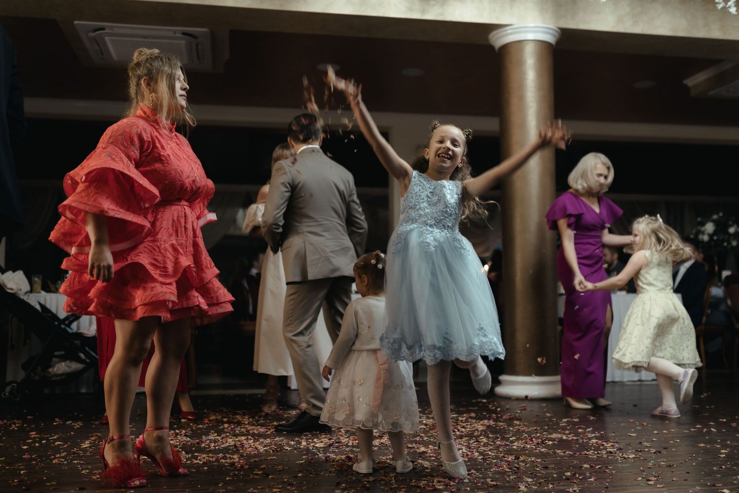 People dancing and twirling on a dimly lit dance floor at a party with formal dresses in red, blue and purple.