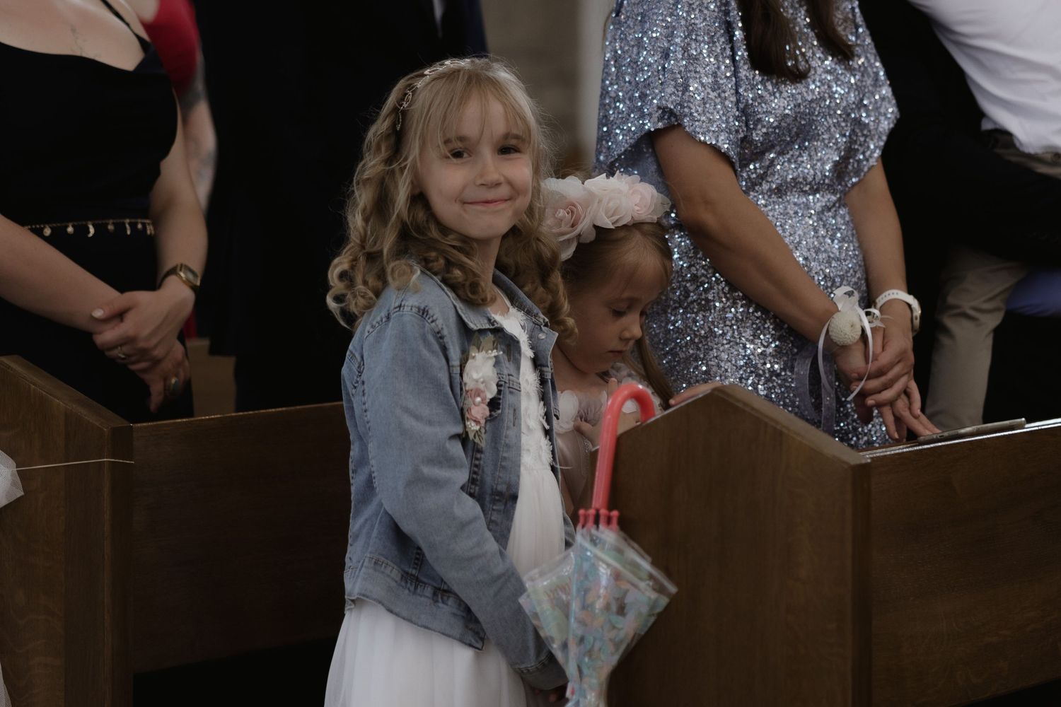 Two children stand among wooden church pews during what appears to be a special occasion or ceremony.