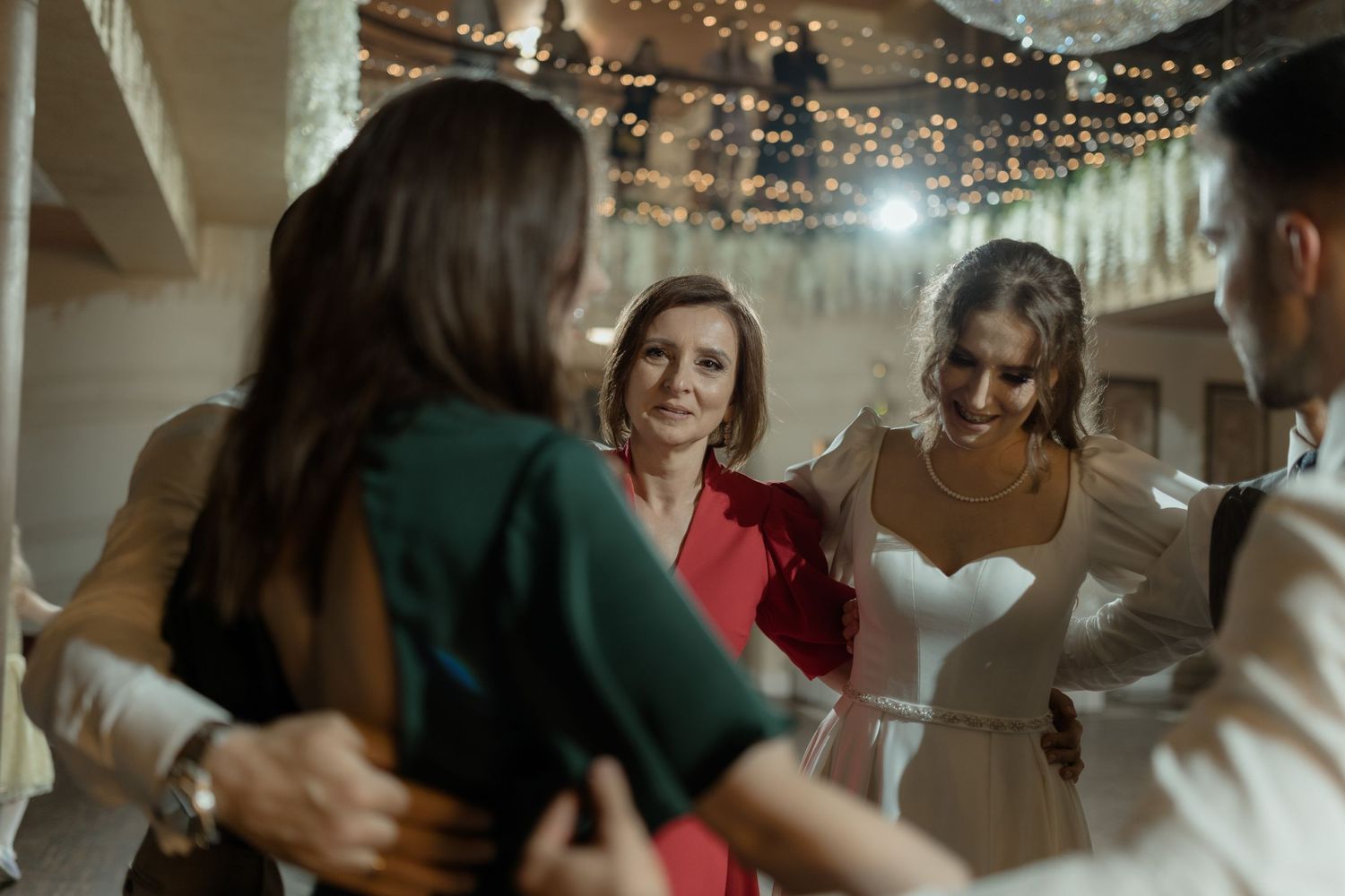 People conversing at an indoor wedding reception under decorative string lights.