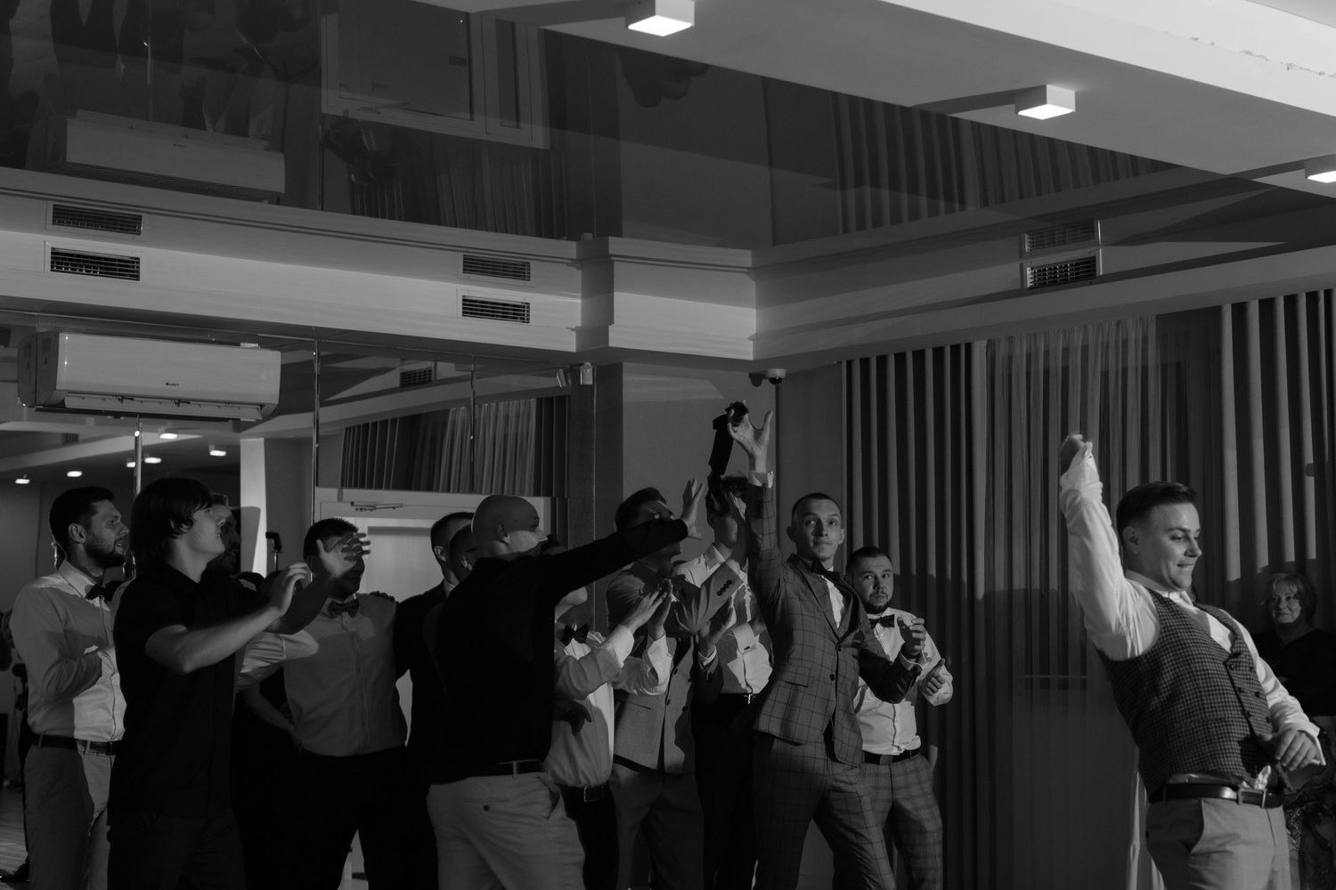 A group of people raise their hands and cheer enthusiastically in what appears to be an indoor venue.