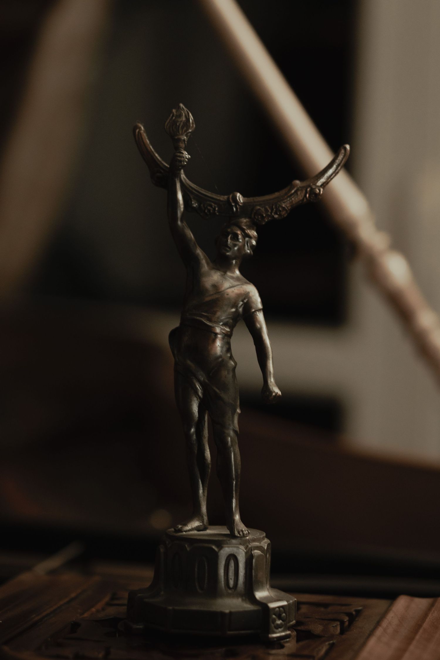 A vintage bronze trophy or statue featuring an athletic figure with raised arms, photographed in moody lighting on a wooden surface.