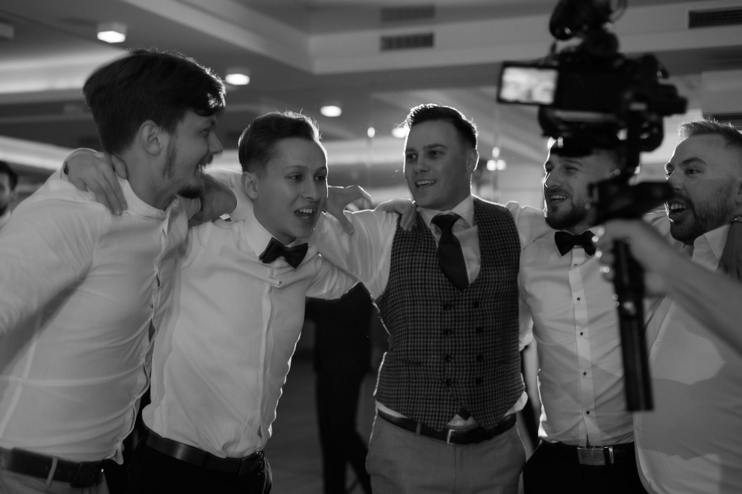 A group of friends in formal attire share a lighthearted moment together in a black and white photo.