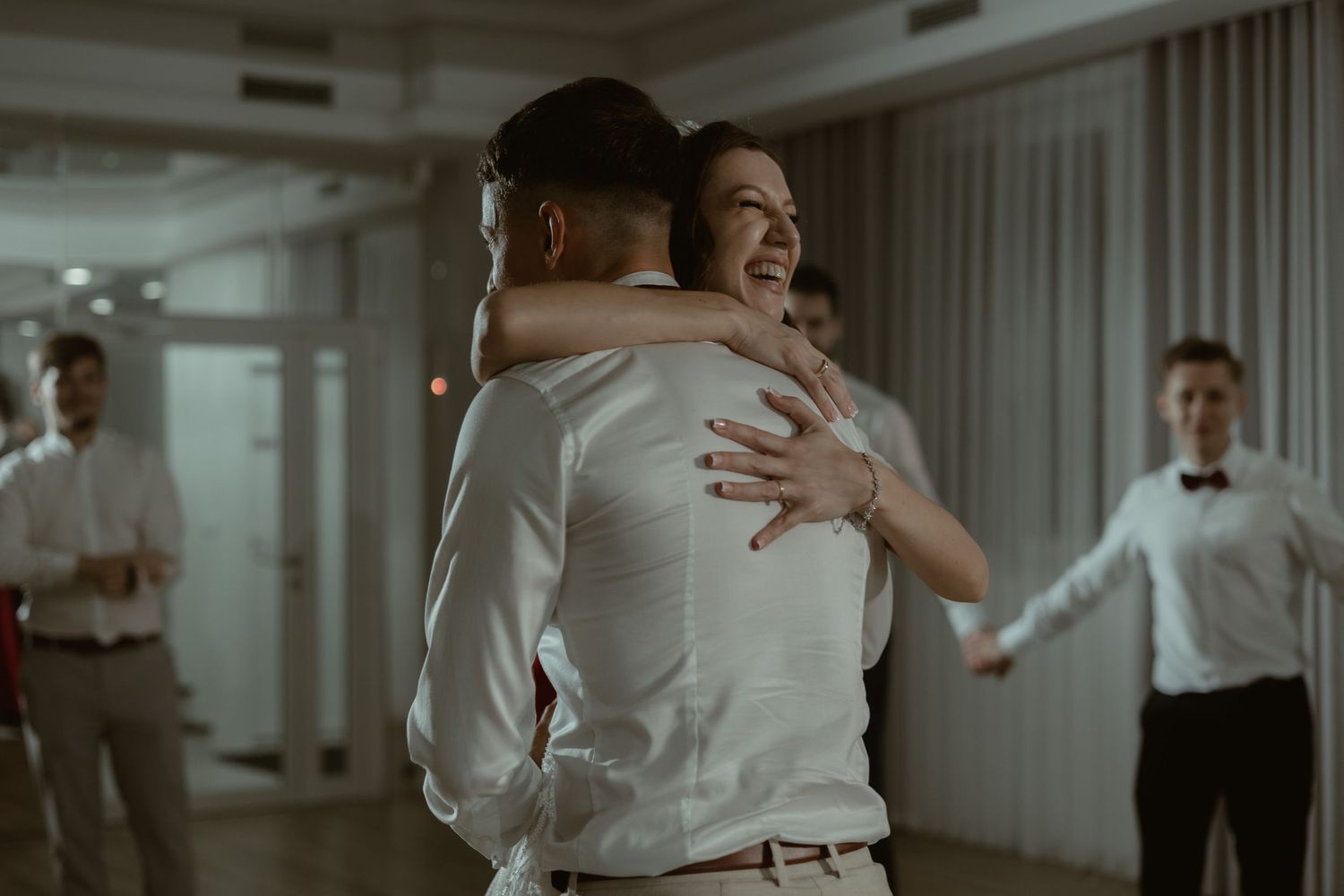 Two individuals share a joyful embrace while dancing at a reception as others look on in the background.