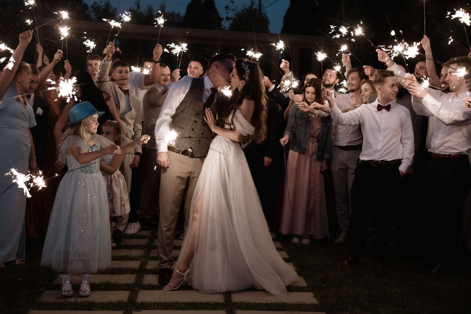 Wedding guests wave sparklers at night during a magical outdoor wedding reception celebration.