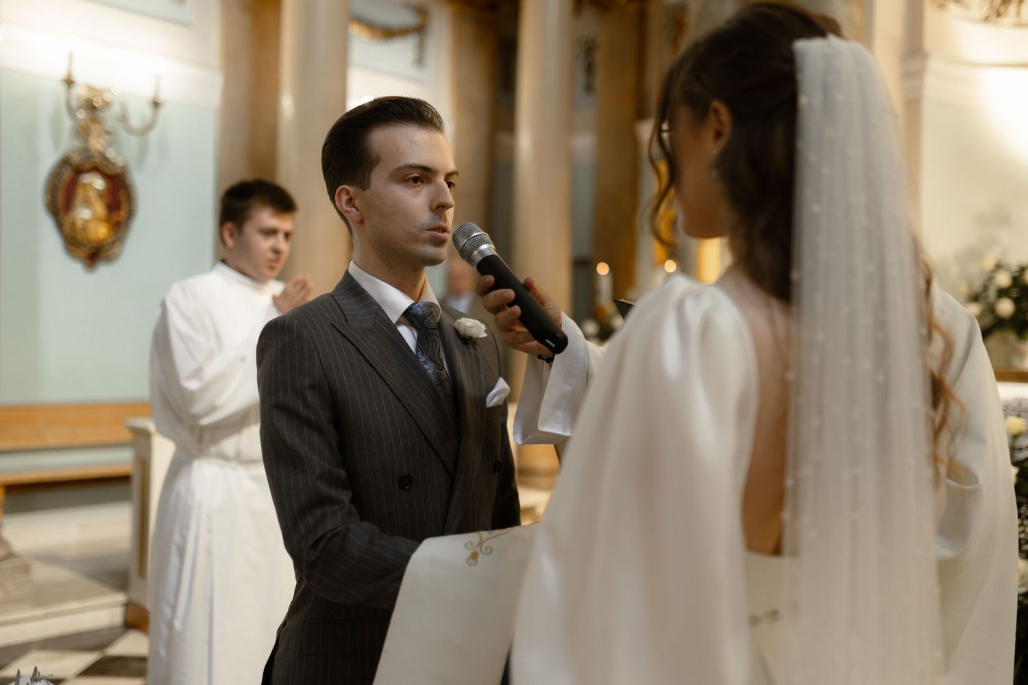 A bride and groom exchange wedding vows during an elegant indoor ceremony at a beautifully lit church.