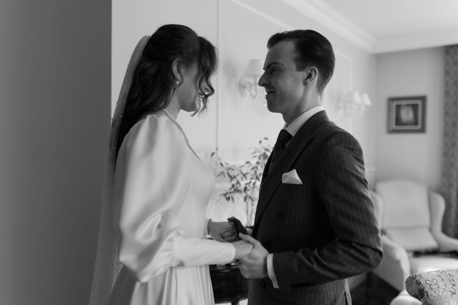 A couple shares an intimate black and white moment together in a room with a window and framed art on the wall.
