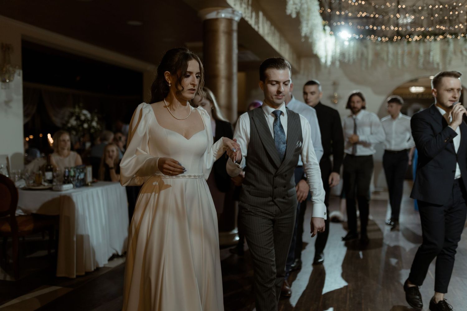 Happy couple celebrates on the dance floor at their wedding reception in a dimly lit venue with string lights.