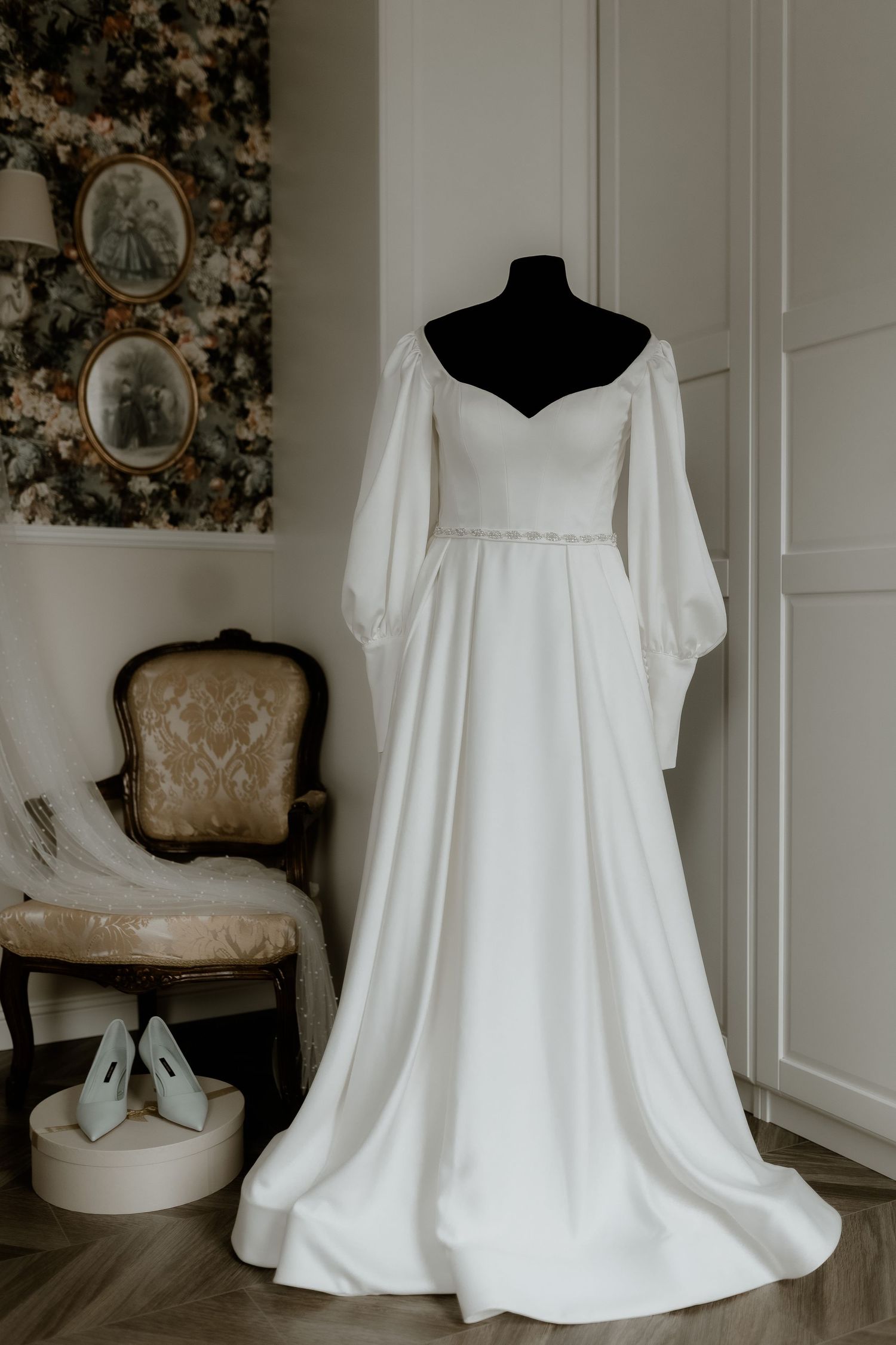 Elegant white wedding dress with puff sleeves and sweetheart neckline displayed on mannequin in vintage-styled room.