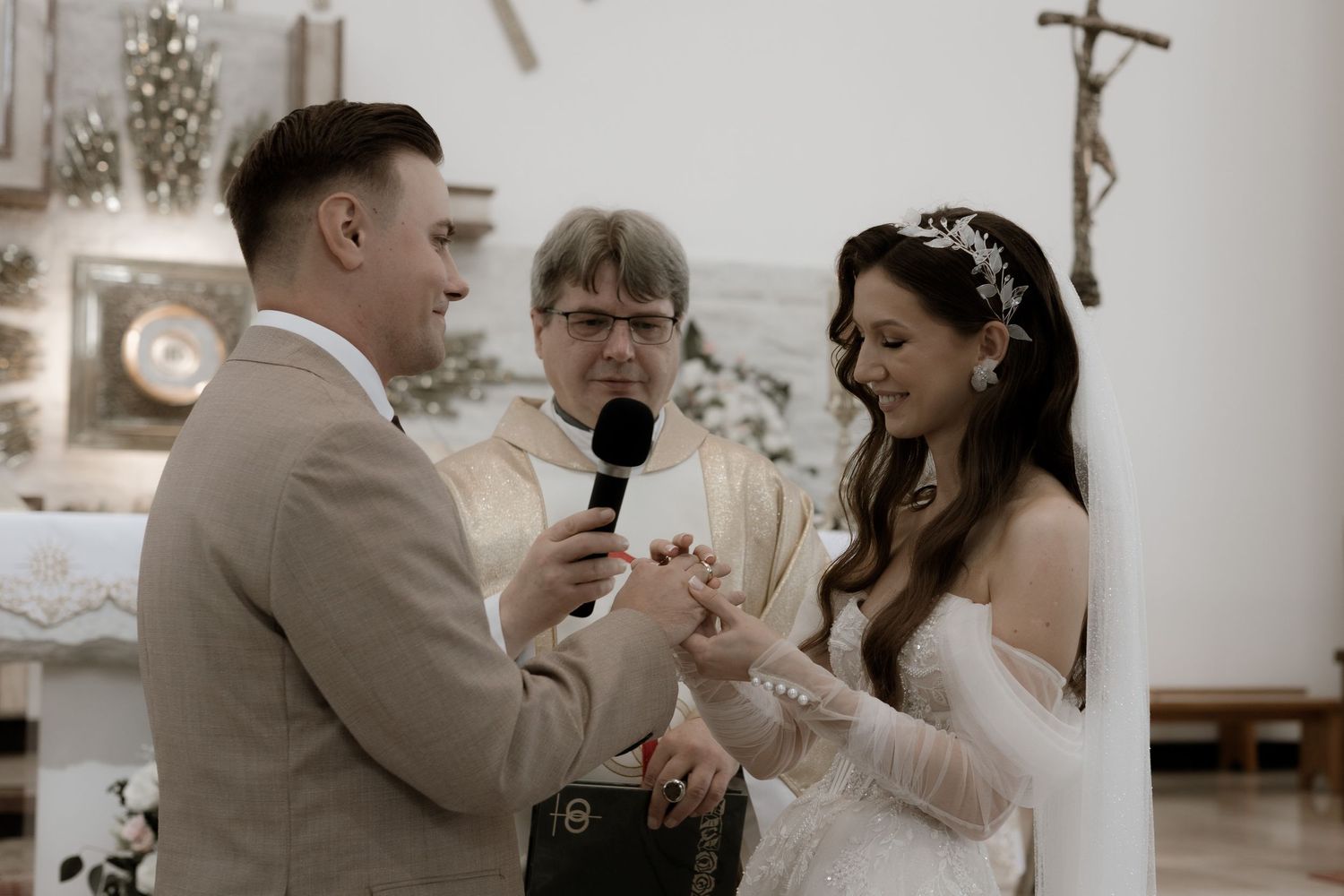 A couple exchanging rings during their wedding ceremony in a church with an officiant present.