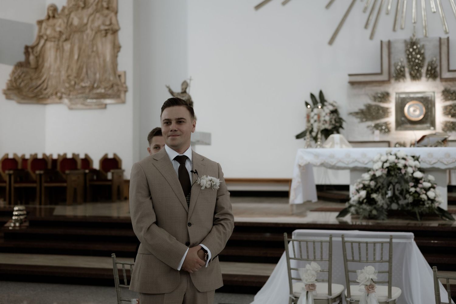 Well-dressed groom stands alone at the altar of an elegant church sanctuary during a wedding ceremony.