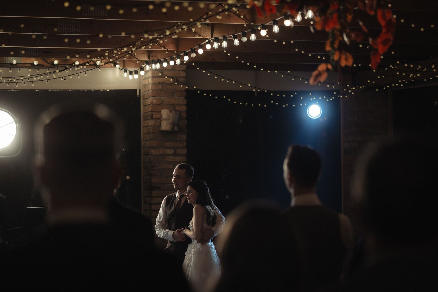 String lights illuminate a dark outdoor venue with a festive atmosphere as silhouettes of people dance and celebrate.
