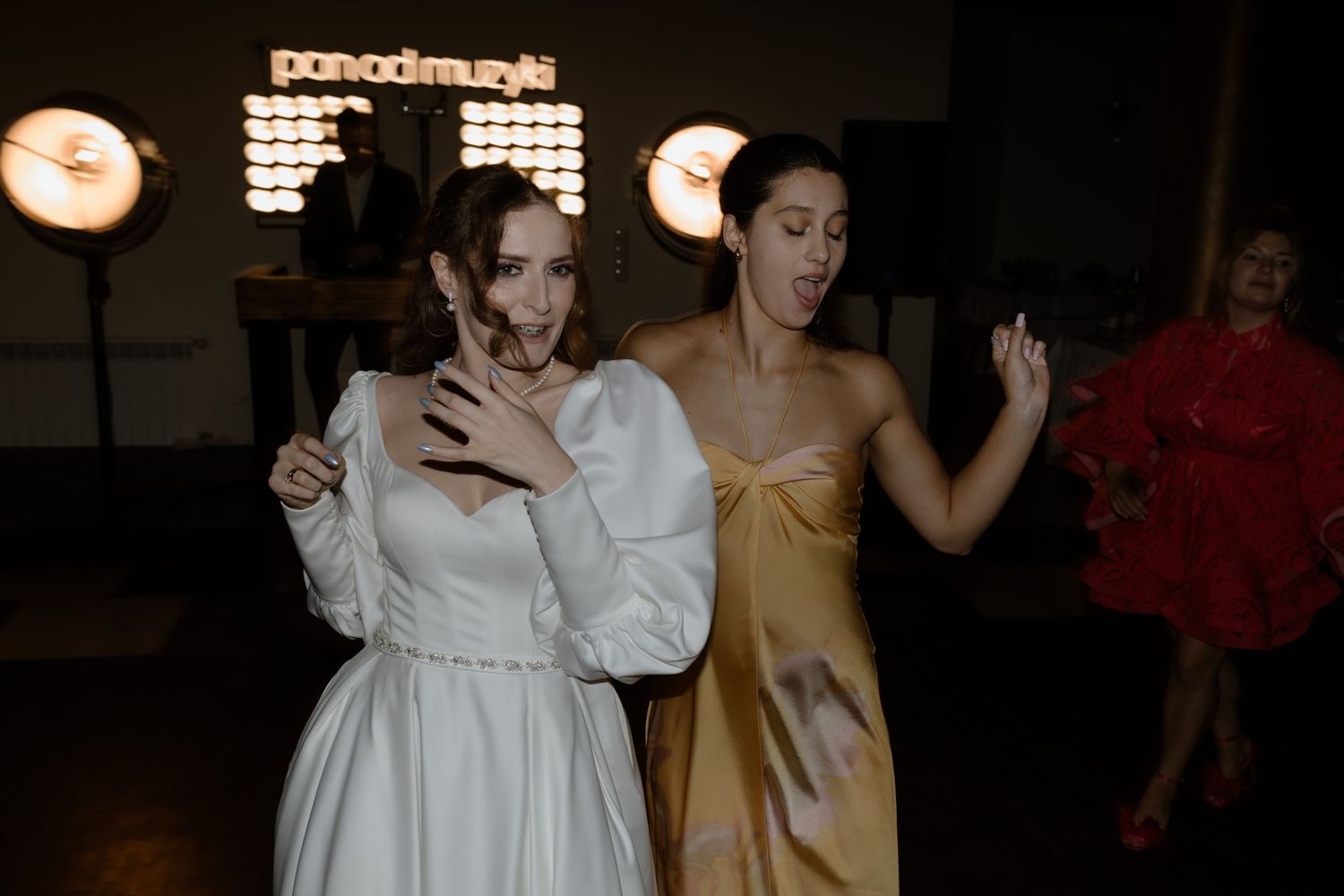 Two people in formal attire dance expressively at a dimly lit event, one in white and one in gold.