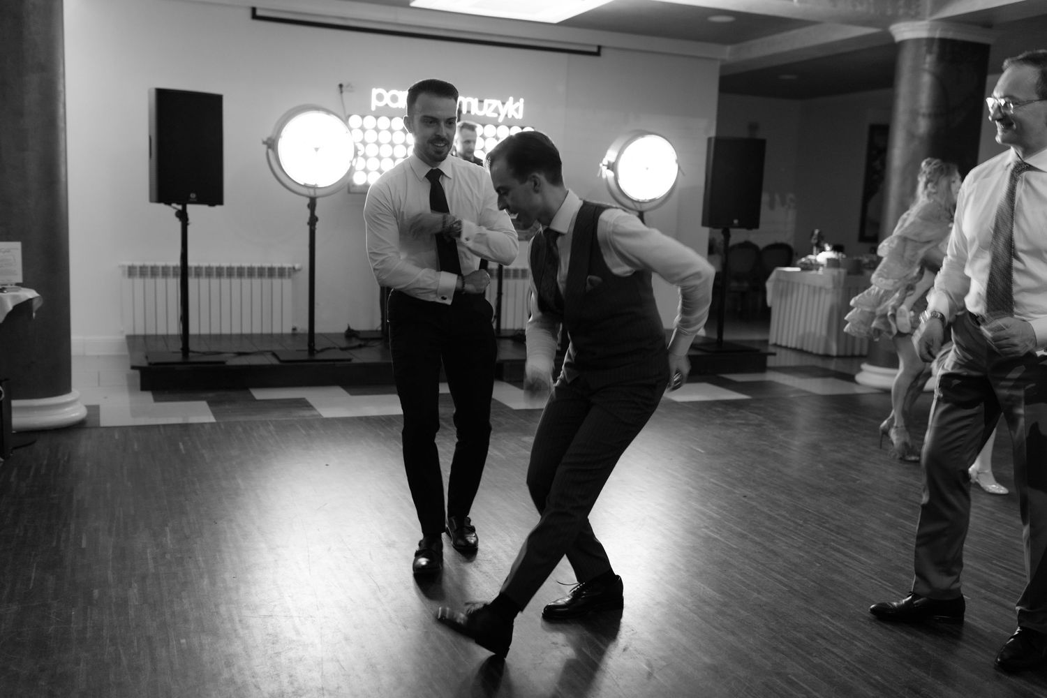 People dancing together at a social event in a monochrome photograph on a wooden dance floor.