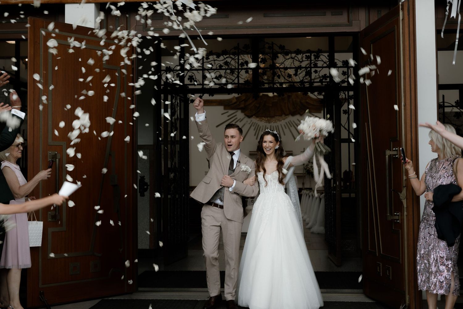 A couple exits their wedding ceremony while guests toss white confetti at their doorway exit.