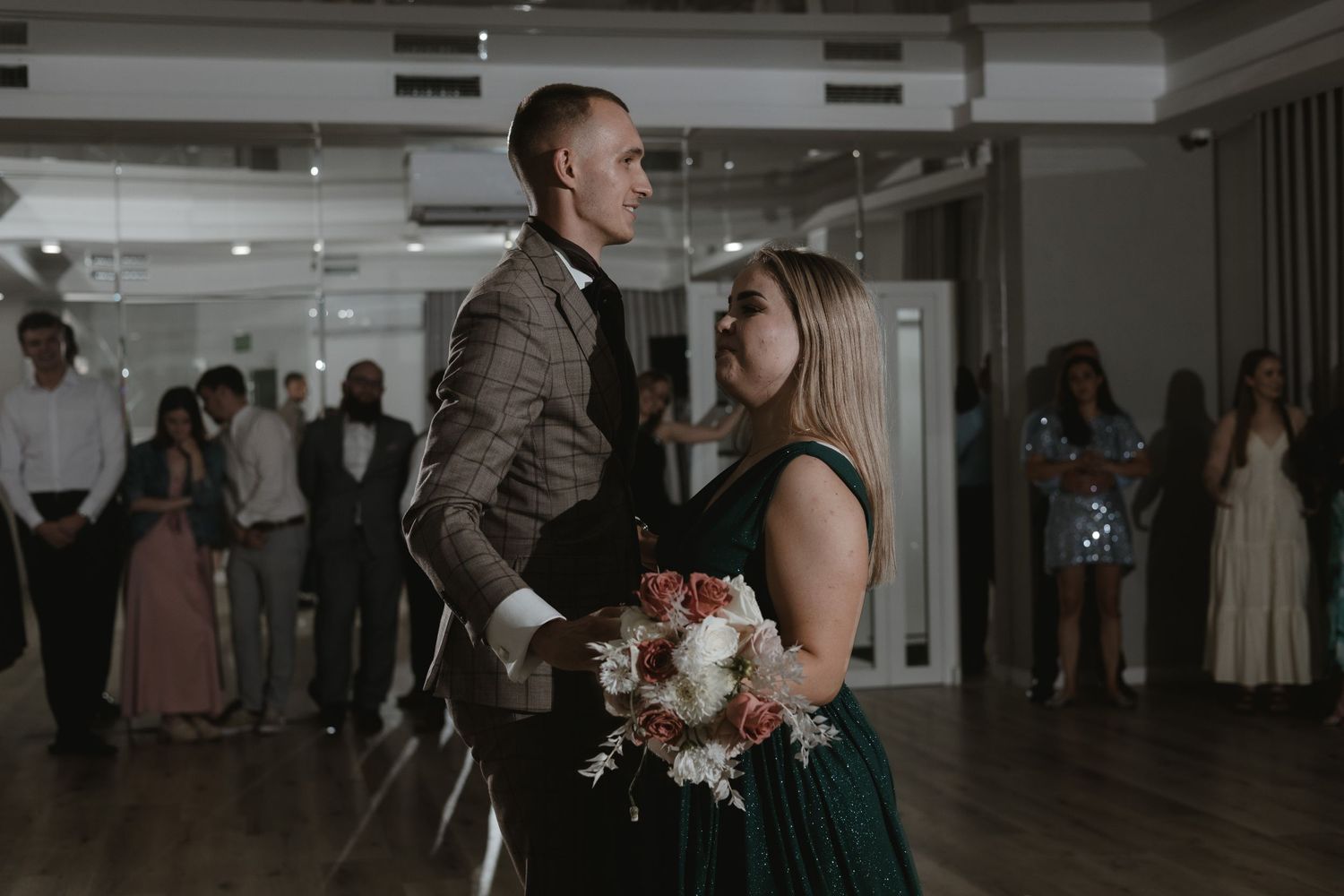 A couple shares an intimate moment while slow dancing at a wedding reception in a dimly lit ballroom.