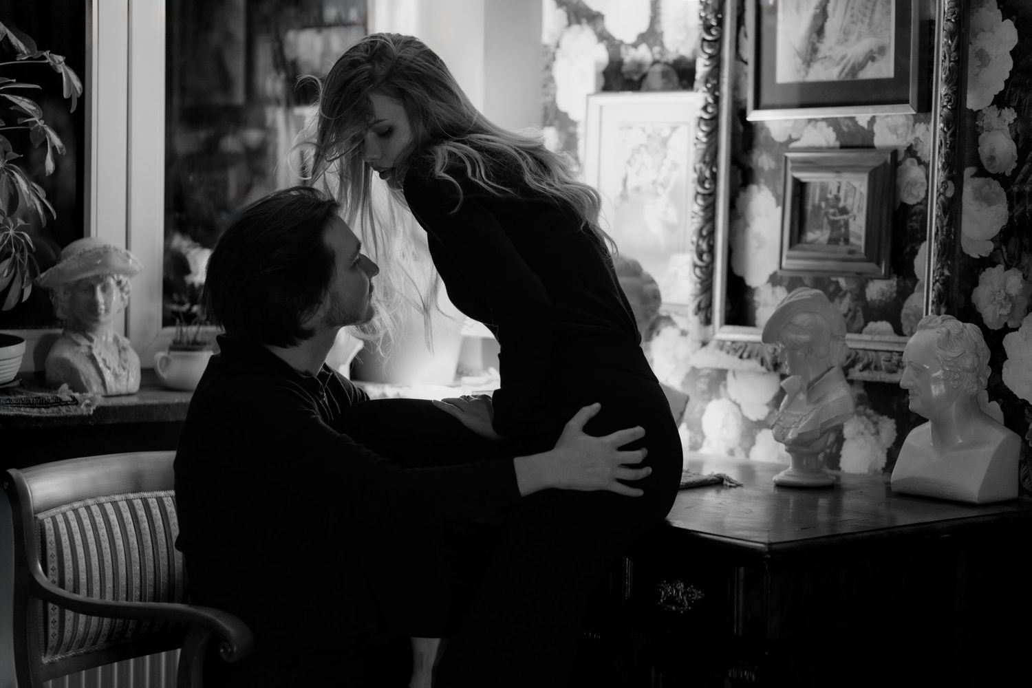 A romantic black and white photograph capturing an intimate moment between a couple in an antique-filled room.