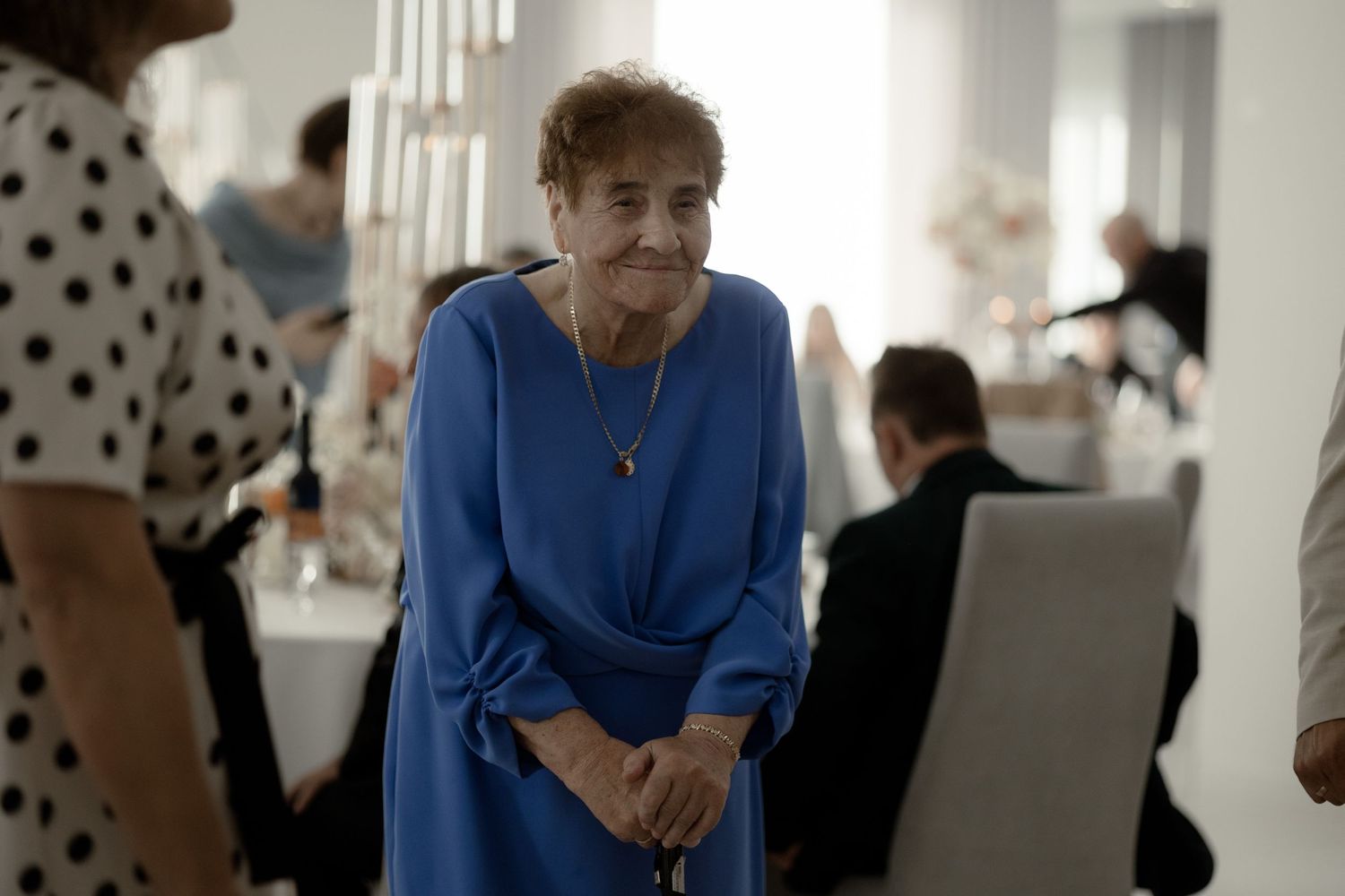 A person in a bright blue dress stands in conversation at an indoor social gathering.