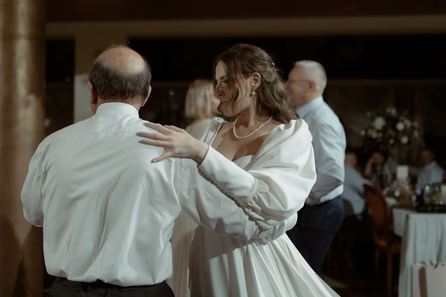A couple dances together at a wedding reception while wearing white formal attire.