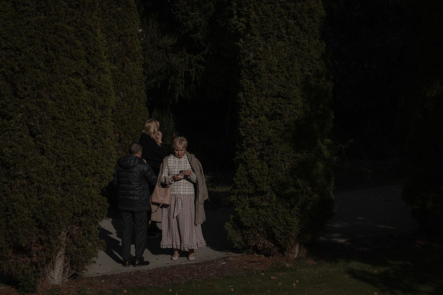 A couple walks through a lush garden pathway with tall hedges on either side during daytime.
