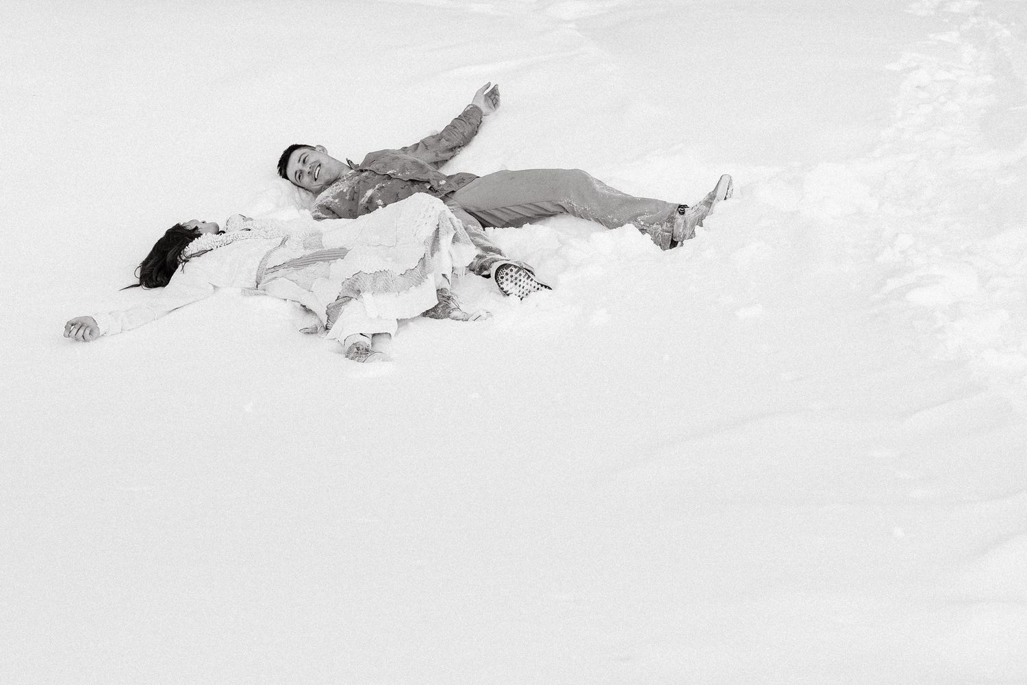 A sight of someone lying in fresh snow making a snow angel with arms and legs spread wide.