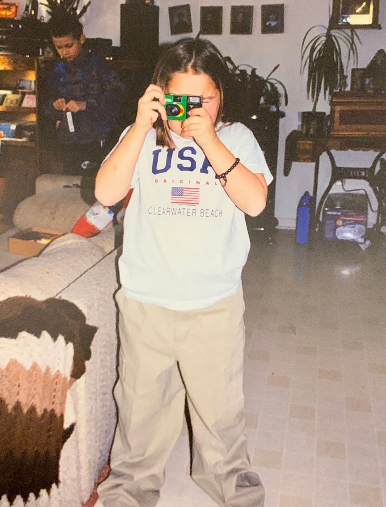 Child in USA shirt and khaki pants using a bright green toy camera inside.