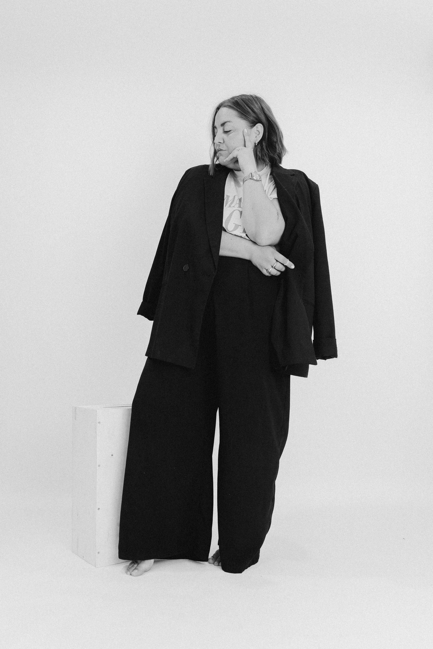 A figure poses in an artistic black and white portrait series wearing a black blazer against a light background.